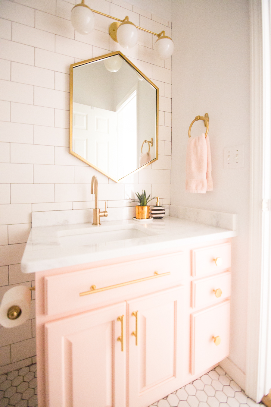 Love this gold hexagon mirror with blush pink cabinets and gold hardware! Such a pretty pink bathroom with gold orb sconces!