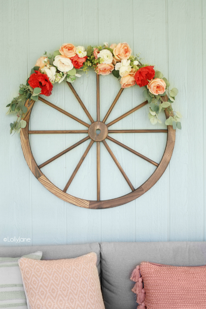 Love this DIY wagon wheel wreath, such a fun summer decoration! Pretty summer wall decor using a wagon wheel and faux florals. #wreath #howto #diy #wagonwheelwreath #diywreath #summerwreath