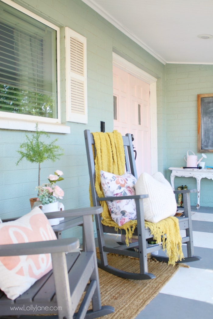 Rocking chairs are a perfect conversation place on your farmhouse porch. A potted topiary, floral pillows and a comfy throw add sweet rustic touches. #farmhouseporch #colorfulporch #frontporchliving #polywood #farmhouserockingchairs #grayrockers #xbackfurniture #farmhousefurniture