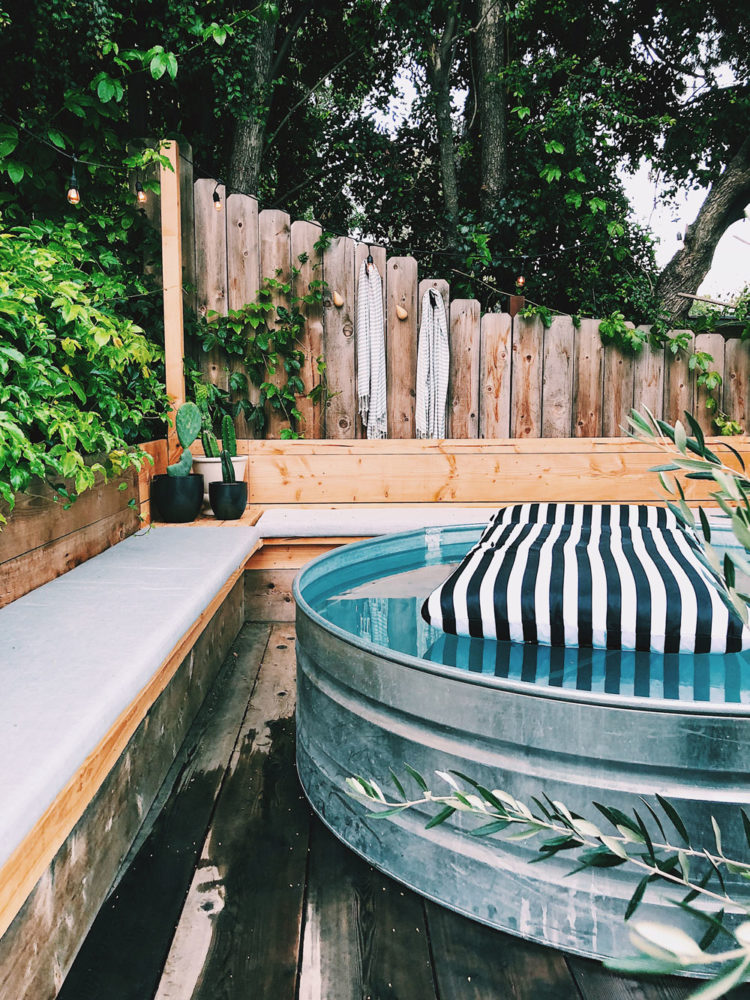 DIY galvanized stock tank pool aka cowboy pool diy and it's anything but! Love this stock pool set on a deck with cozy cushions on a wood bench with pretty outdoor hanging lights, so pretty! #stocktankpool #cowboypool #hillbillypool #diypool