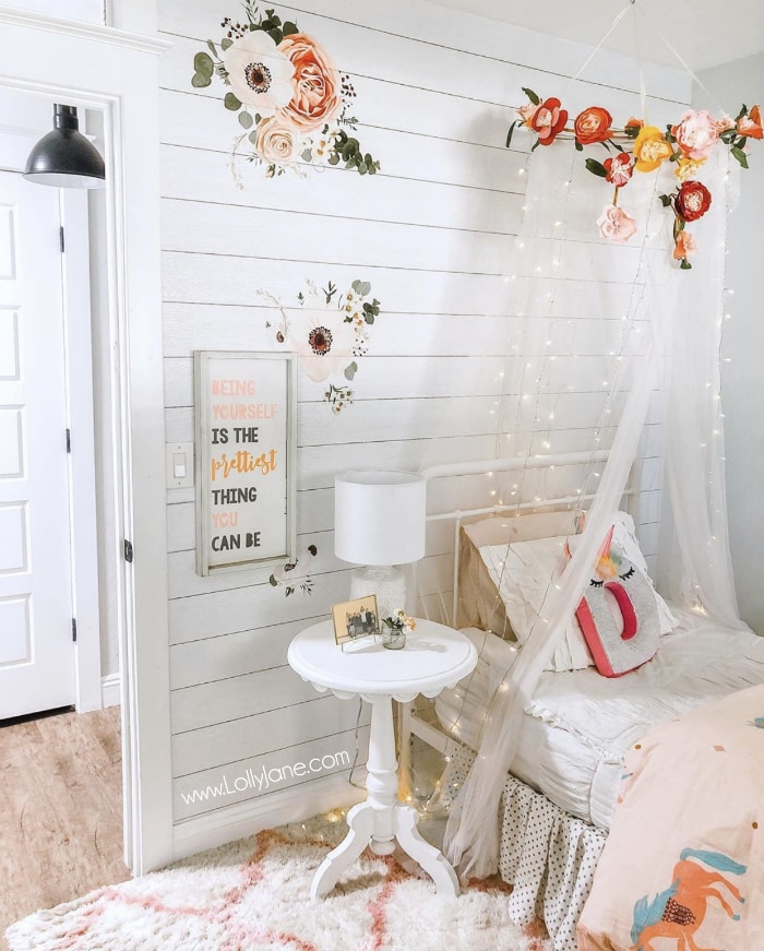 Create this diy floral canopy with lights from tulle netting with lace, a fake flower bunting and curtain Fairy lights. Add this dome tent to your girls rooms for a cozy spot to curl up in. #fairylights #girlsroomdecor #girlroomdecorations #canopylights #canopybed #floralcanopybed #girlsroomcanopy #bedcanopy #diybedcanopy