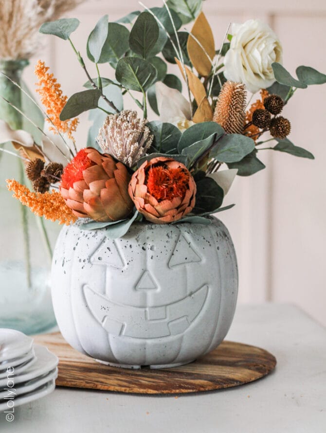 Easy decoration idea! Pour concrete into a $1 pumpkin pail, so cute and makes the PERFECT centerpiece for Halloween or fall! #fallfloralarrangement #fallflowers #pumpkinplanter