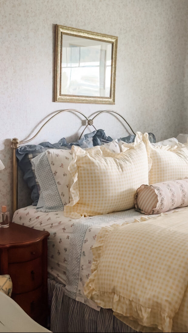 Queen bed styled with floral cottagecore bedding, layered pillows, and soft neutral linens