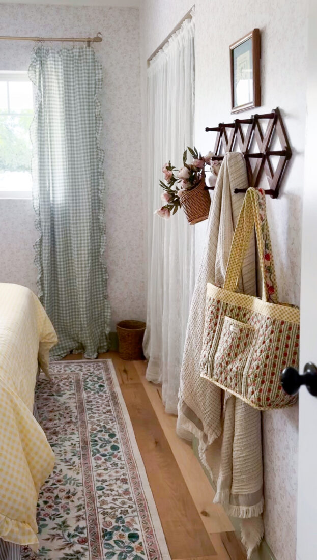 Wooden accordion wall rack in a cozy cottage-style guest bedroom used to hang blankets, robes, and decorative accessories
