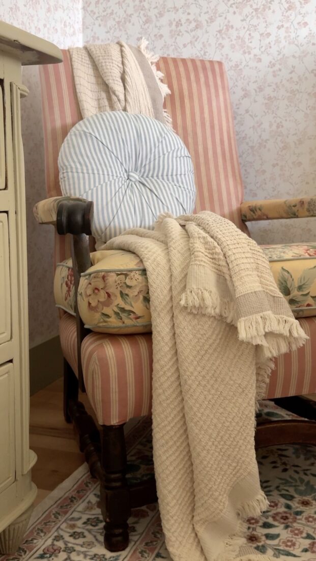 Vintage thrifted chair with floral pillow beside a dresser in a cozy cottage guest room